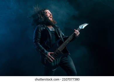 Expressive rock guitar man player with long hair and beard plays on the black background. Smoke background. Studio shot. 