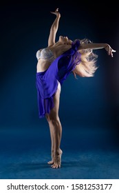 Expressive And Sensual Girl Dancer In A Jump And A Beautiful Pose In The Fog On A Blue Background