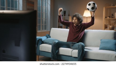 Expressive Spain man football team supporter emotionally watching a soccer game. Hipster guy with curly hair watching tv at home alone  - Powered by Shutterstock