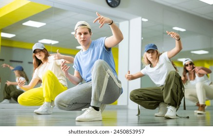 Expressive teen boy and three teenagers in caps sitting in breakdance pose in dance hall - Powered by Shutterstock