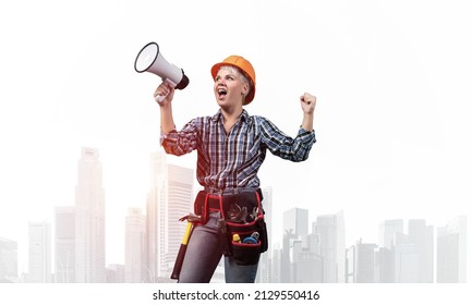 Expressive Woman In Safety Helmet Shouting Into Megaphone. Portrait Of Young Emotional Construction Worker With Wide Open Mouth On Foggy City Background. News Announcement And Advertisement.