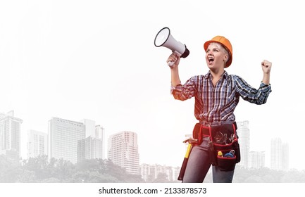 Expressive Woman In Safety Helmet Shouting Into Megaphone. Portrait Of Young Emotional Construction Worker With Wide Open Mouth On Foggy City Background. News Announcement And Advertisement.