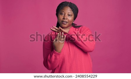 Expressive young black woman showing time-out sign using her hands in front of pink background. African american beauty displaying pause-break signal with body language towards camera.