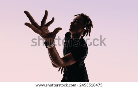 Expressive young man with dreadlocks dances energetically in a studio to the rhythm of a song. His eyes closed, hands in motion, he listens with wireless earbuds and a smartwatch.