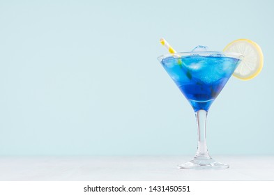Exquisite blue cocktail for celebration in beach style with blue curacao, ice cube, lemon slice, yellow straw in mint color bar interior on white wood table.