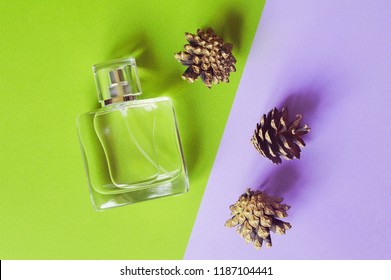 Exquisite Luxury Perfume With A Woody Fragrance On A Green And Purple Background Next To Pine Cones. Flat Lay Beauty Photography. Still Life Close Up Photo. Image For Poster
