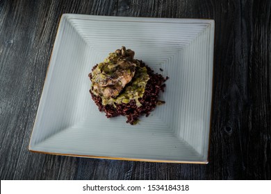 Exquisite Restaurant Dish Of Whole Grilled Quail With Green Onion Dressing Served On Wild Rice On Modern Plate On Dark Wooden Table