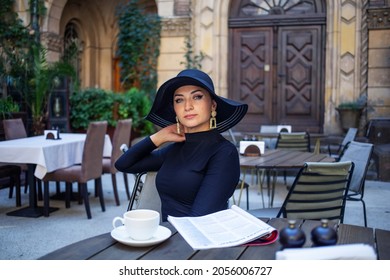 Exquisite Frau in einem schwarzen Hut trinkt Kaffee
