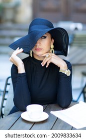 Exquisite young woman in a black hat drinks coffee at cafe 