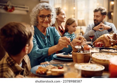 Extended family gathering for meal at dining table on Thanksgiving. Focus is on senior woman talking to her grandson.  - Powered by Shutterstock