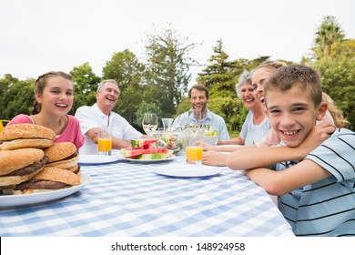 Extended Family Having Dinner Outdoors At Picnic Table Smiling At Camera