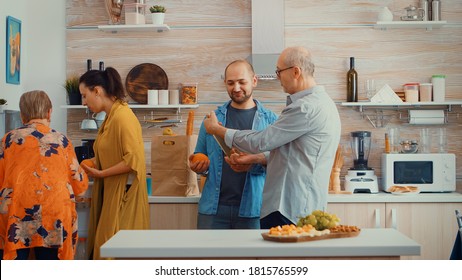 Extended Family Putting The Groceries In The Fridge. Young Couple Coming From Shopping Bringing A Paper Bag With Groceries, Fresh Food From Supermarket At Parents Home To Prepare Family Dinner