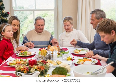 Extended Family Saying Grace Before Christmas Dinner At Home In The Dining Room