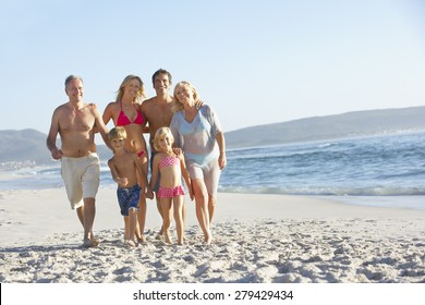 Extended Family Walking Along Sandy Beach By Sea