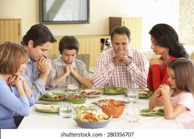 Extended Hispanic Family Saying Prayers Before Meal At Home