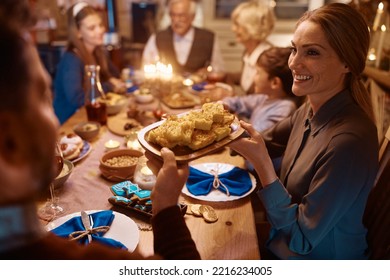 Extended Jewish Family Having Dinner At Dinning Table While Celebrating Hanukkah. Focus Is On Woman Passing Food To Her Husband. 