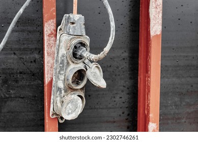 Extension cord, electrical socket, power cord old and damaged on the construction site outside. Extremely dangerous, unsafe to use. Should be replaced. Unsafe workplace