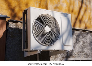 Exterior air conditioning compressor unit installed on a wall, used for cooling and ventilation in residential or commercial buildings, showing modern climate control equipment.