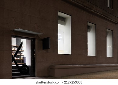 Exterior Of The Beauty Salon With Big Windows And Glass Door In The Old Building In Europe. Entrance Of The Modern Barbershop In The Evening.