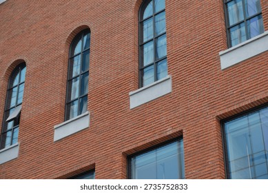 The exterior of a building showcases a repeating pattern of arched windows set against a textured red brick wall, highlighting a blend of traditional and contemporary design elements