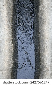 Exterior close up top view photo visual view of a dirty sewer ditch with dark water running down made from concrete and cement aside a paement or road in a street city
