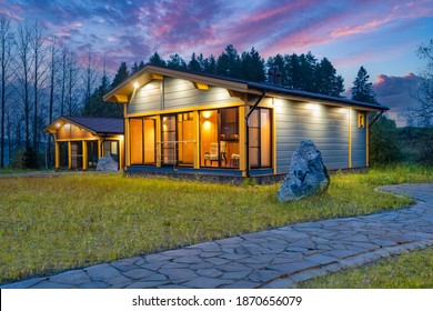 Exterior of a country cottage. Small houses on background of forest. Scandinavian style wooden houses. Lawn and stone path next to cottage. Architectural design of a Scandinavian house. Evening time