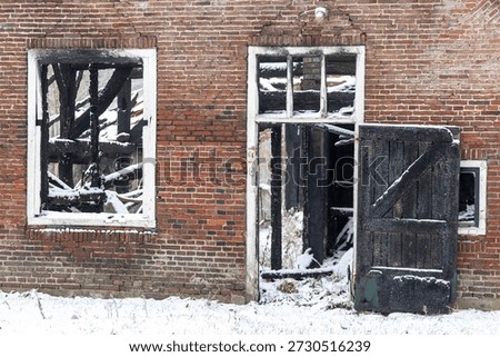 Exterior facade of burned down barn covered in snow after a blizzard snowstorm with the black wood and construction carcas contrasting against the white winter landscape