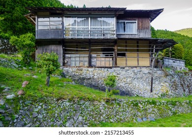 Exterior front view of old Japanese house with large windows and stone foundation in rural mountains