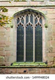 Exterior of a gothic style leaded glass window with diamond lattice pattern and arched stone frame. At Saint Mary and All Saints' Church in Great Budworth village, Cheshire, England 