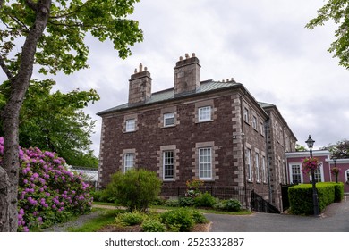 The exterior of Government House, the residence of the Lieutenant Governor of Newfoundland. The walls are made of red sandstone with English portland stone trim, a mansard roof, and a lush garden. - Powered by Shutterstock