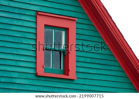 The exterior of a green wooden clapboard building with a peaked cedar shake roof. The wood wall is horizontal cape cod beveled clapboard siding. The barn has a small single hung window with red trim.