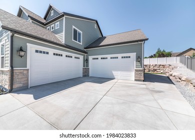 Exterior of a house with concrete driveway and two closed white garage doors with windows. Side view of a gray large house with bricks and rock landscape and fence on the side. - Shutterstock ID 1984023833