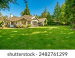 Exterior image of a single story rambler home painted white wiht a very large driveway and three car garage large backyard lush landscaping and foilage on a summer day blue skies