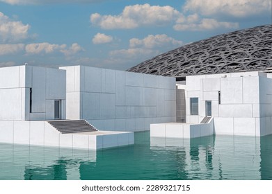 Exterior of Louvre Abu Dhabi famous museum. Plain white walls surrounding an emerald green moat topped with an ornate dome roof