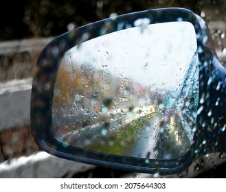 Exterior Mirror Of A Car In The Pouring Rain With A Blurred View Of Road Users