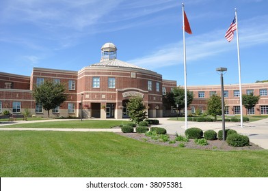 exterior of a modern American high school building with the American flag on the flag pole and a lush green lawn