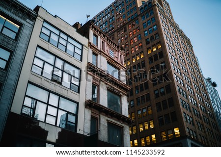 Exterior of modern constructed real estate with lights in office windows located in downtown, tall buildings with rental apartments for residents and commercial property for corporation and companies