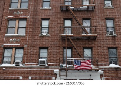 Exterior Of An Old Brick Apartment Building With An American Flag And Fire Escapes With Snow During The Winter In New York City