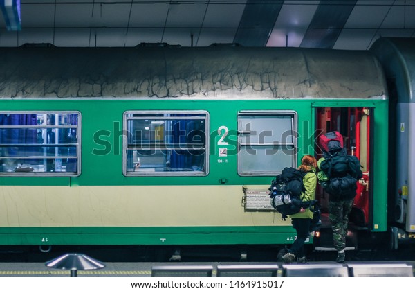 Exterior of Polish green sleeping\
train wagon, standing on a platform on a train station in Krakow\
with backpackers going aboard. Backpack traveling with a\
train.