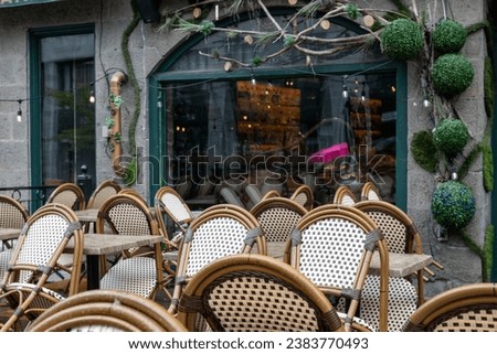 The exterior seating area of an empty restaurant or bistro. The tables are in rows with rattan chairs tipped over the edge of the tables. There's a black fence around the garden eating area.