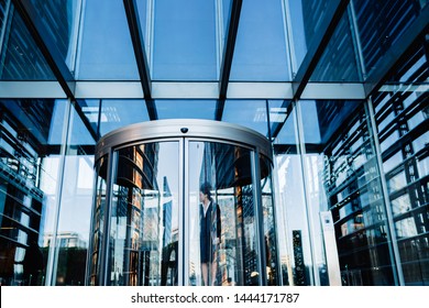 Exterior Of Shiny Contemporary Facade Of Office Building With Glass Revolving Doors And Coworkers Walking Out On Street In Daylight