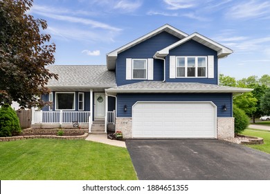 Exterior Of A Suburban Home With Blue Siding, A White Front Porch, And White Shutters.