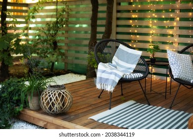Exterior veranda of house with black Acapulco armchairs and plants pots. Cozy space in patio or balcony with garland. Interior Wooden verande with garden furniture. Modern lounge outdoors in backyard - Shutterstock ID 2038344119
