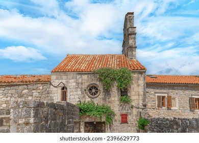 Exterior view of the Church of Santa Maria in Punta in Budva Old Town, Montenegro. Facade of an ancient stone building with a red tiled roof and a round window. Flowering caper bushes grow on the wall - Powered by Shutterstock