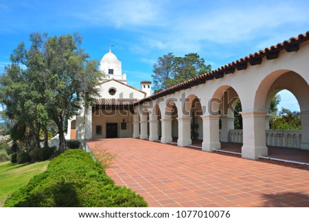 Exterior view of the Junipero Serra Museum in the Presidio Park of San Diego with the arched entrance walk way, the Terracotta tiled floor and the Spanish Colonial historic fort in the background.