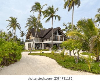 Exterior view of the lobby or reception building on a tropical island in the Maldives surrounded by a garden with palm trees. - Powered by Shutterstock