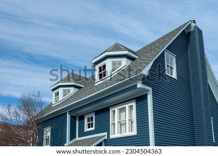 The exterior view of two polygonal dormers on a modern blue rooftop of a wooden house. The multi-sided dormers have three double-hung windows on a sloping roof of grey shingles with a blue sky behind. ストックフォト © 