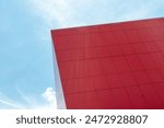 The exterior wall of a contemporary commercial style building with aluminum metal composite panels. The futuristic corner of a bright red building has engineered diagonal cladding steel frame panels. 