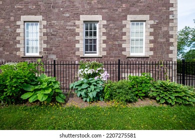 The Exterior Wall Of A Large Brown Block Vintage Building With Three Tall Closed Glass Windows With Multiple Panes And Curtains. The Windows And Building Corner Have Decorative Tan Colored Molding.