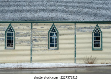 The Exterior Wall Of A Religious Building With Pale Yellow Colored Narrow Horizontal Clapboard Siding And Tall Gothic-style Windows With Clear Glass, White Wooden Muntins, And Green Wood Trim. 